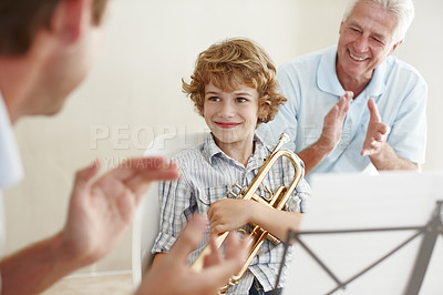 Buy stock photo Shot of a cute little boy looking pleased as his father and grandfather cheer him on after playing the trumpet