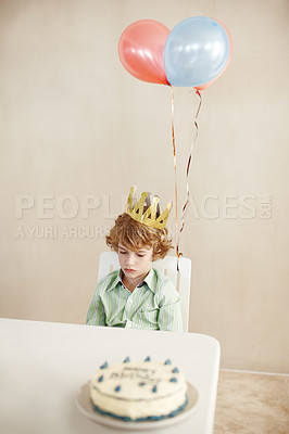Buy stock photo Shot of a cute little boy looking unhappy while sitting at a table with his birthday cake