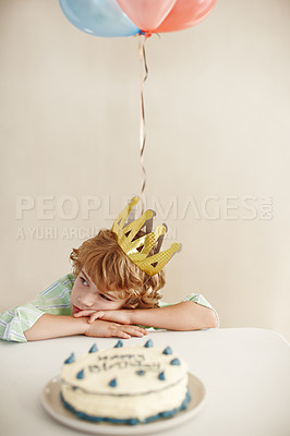 Buy stock photo Shot of a cute little boy looking unhappy while sitting at a table with his birthday cake