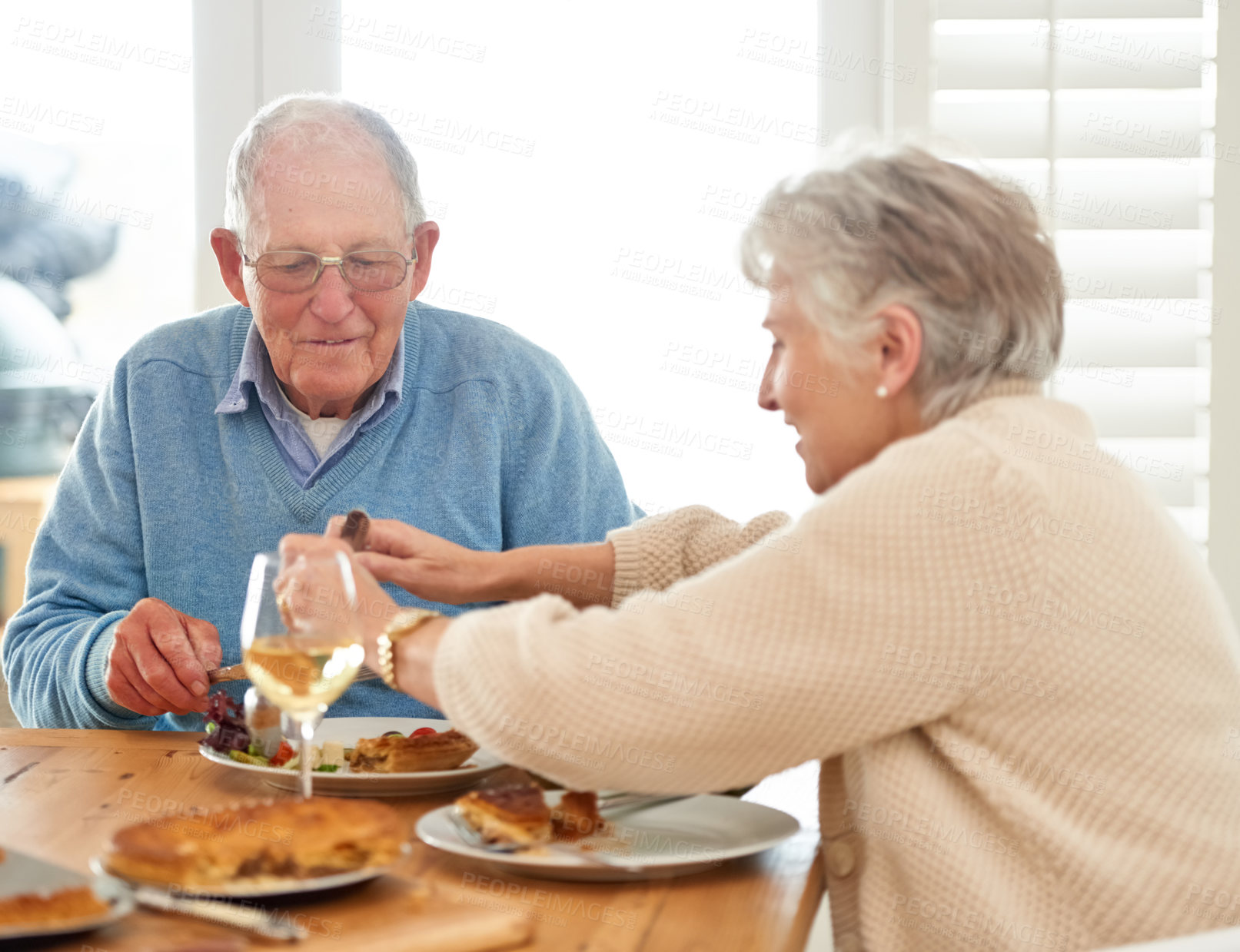 Buy stock photo Love, help and senior couple eating lunch together in the dining room of their modern home. Happy, date and elderly man and woman in retirement talking, bonding and enjoying meal or food in a house.