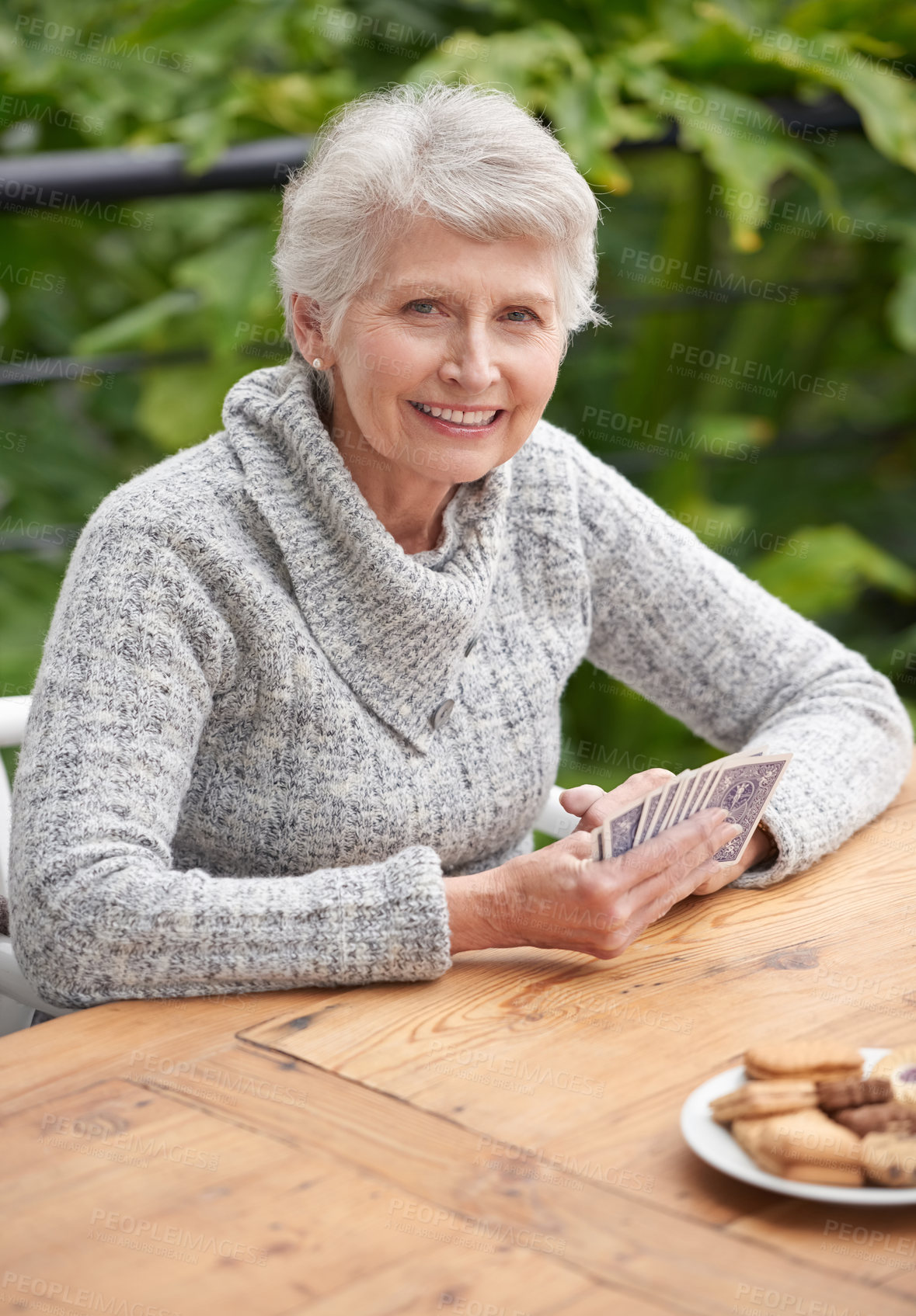 Buy stock photo Elderly woman, cookies and portrait with cards at table for relaxation, old age and retirement. Senior person or grandmother and smiling with wrinkles for poker game, gamble and hobby for leisure