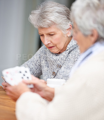 Buy stock photo Senior women, thinking and playing cards with game for friends in retirement, relax and bonding together. Elderly people, poker and strategy with serious fun at table in nursing home for weekend.