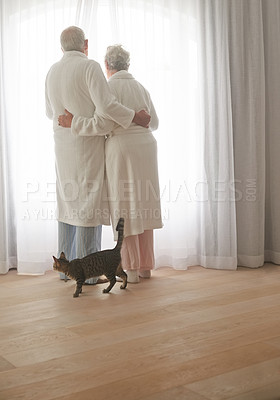 Buy stock photo Shot of a senior couple in bathrobes looking out of a window