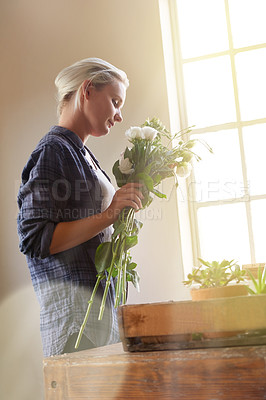 Buy stock photo Shot of a young woman holding a bunch of flowers while standing by a window indoors