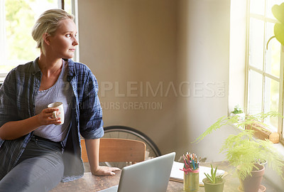 Buy stock photo Shot of a young woman looking thoughtful while sitting on her desk drinking coffee