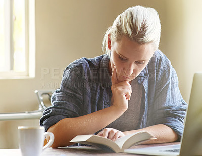 Buy stock photo Shot of a young woman looking thoughtful while reading a book at her desk