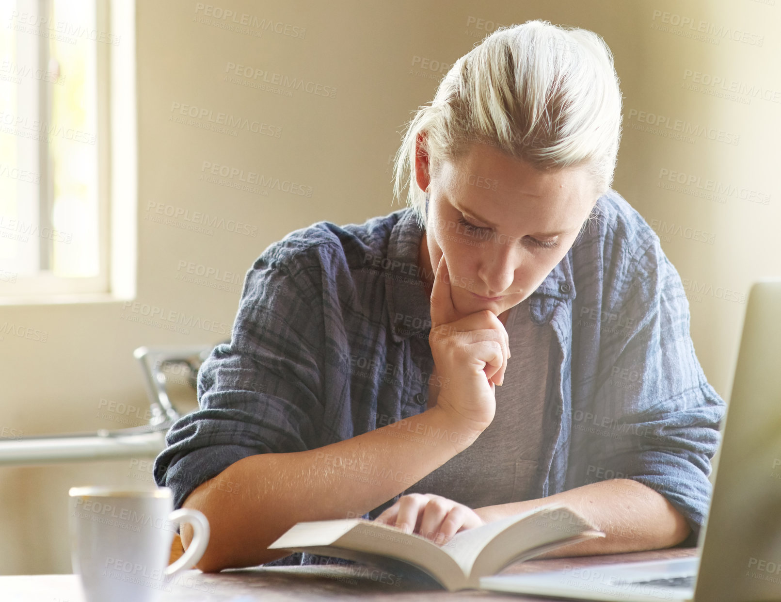 Buy stock photo Shot of a young woman looking thoughtful while reading a book at her desk