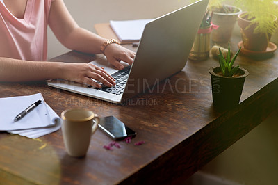 Buy stock photo Cropped shot of a woman working on her laptop with a pen and notebook beside her