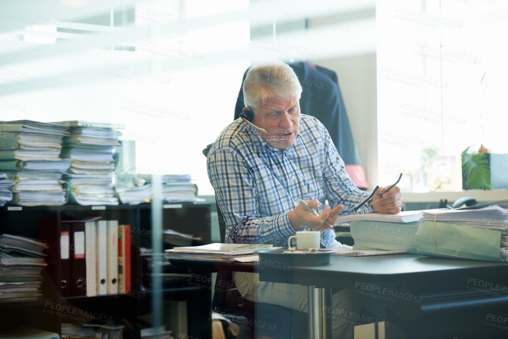 Buy stock photo A senior businessman wearing a headset discussing work while sitting at his office desk