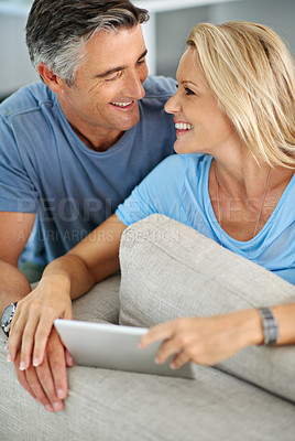 Buy stock photo Shot of a smiling couple sitting at home using a digital tablet