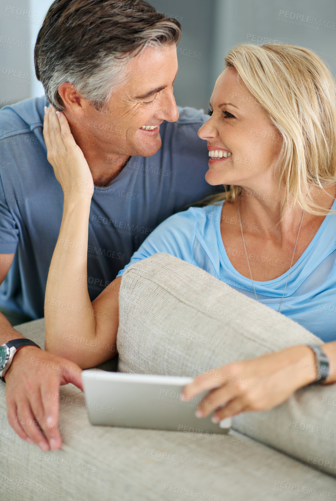 Buy stock photo Shot of a smiling couple sitting at home using a digital tablet