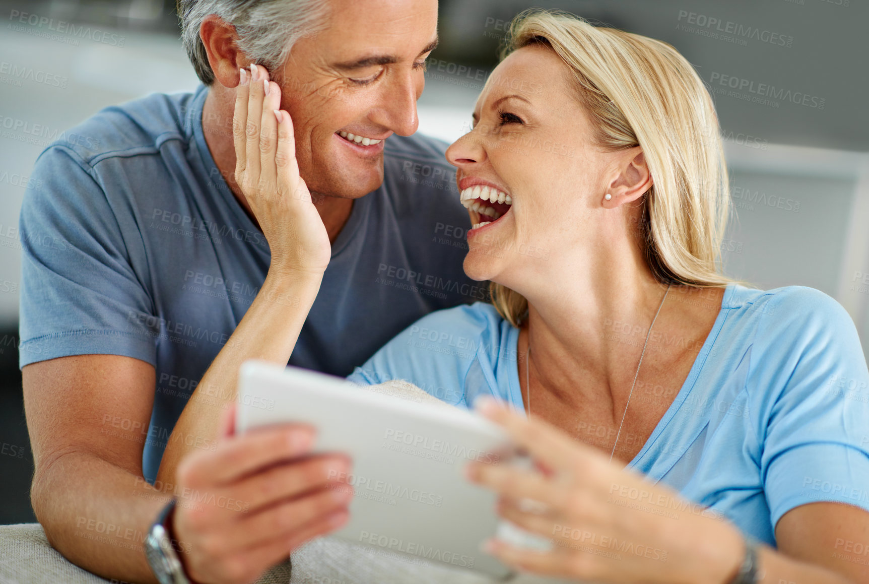 Buy stock photo Shot of a laughing couple sitting at home using a digital tablet