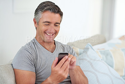 Buy stock photo Shot of a handsome mature man using his phone while relaxing at home