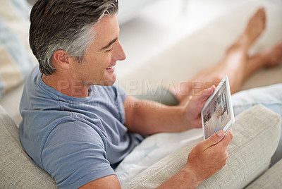 Buy stock photo Shot of a handsome mature man using a digital tablet while relaxing at home