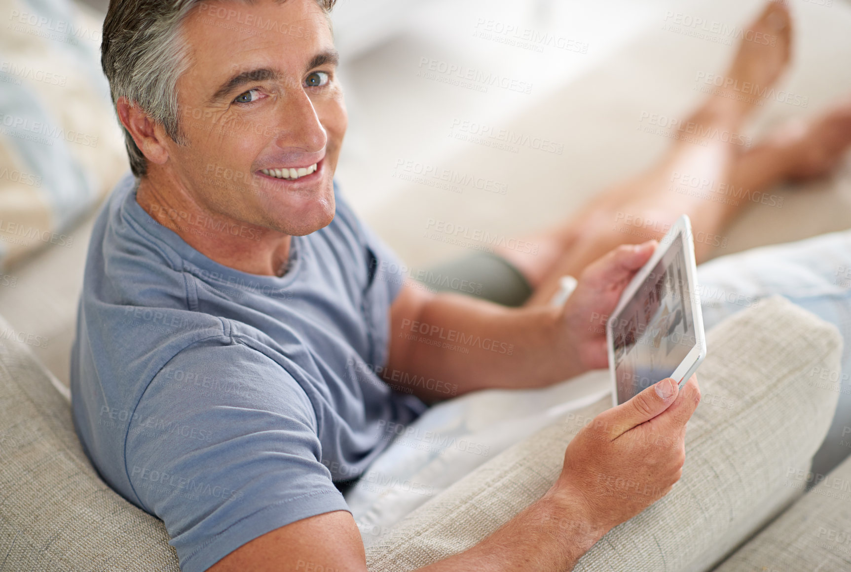 Buy stock photo Portrait of a handsome mature man using a digital tablet while relaxing at home
