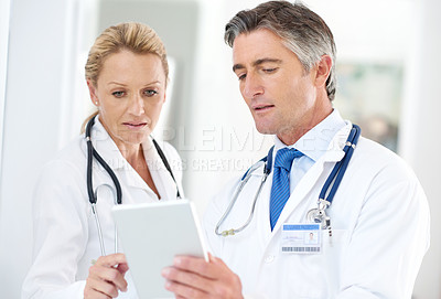 Buy stock photo Shot of two doctors talking together over a digital tablet in a hospital