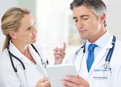 Buy stock photo Shot of two doctors talking together over a digital tablet in a hospital