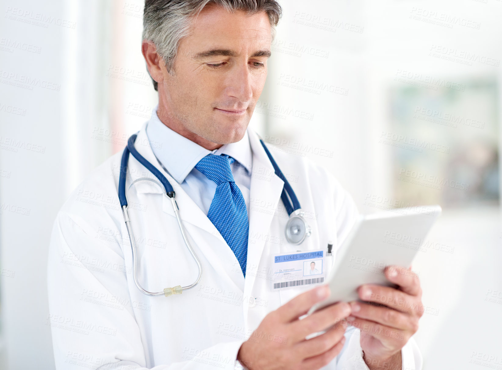 Buy stock photo Shot of a doctor holding a digital tablet while standing in a hospital corridor