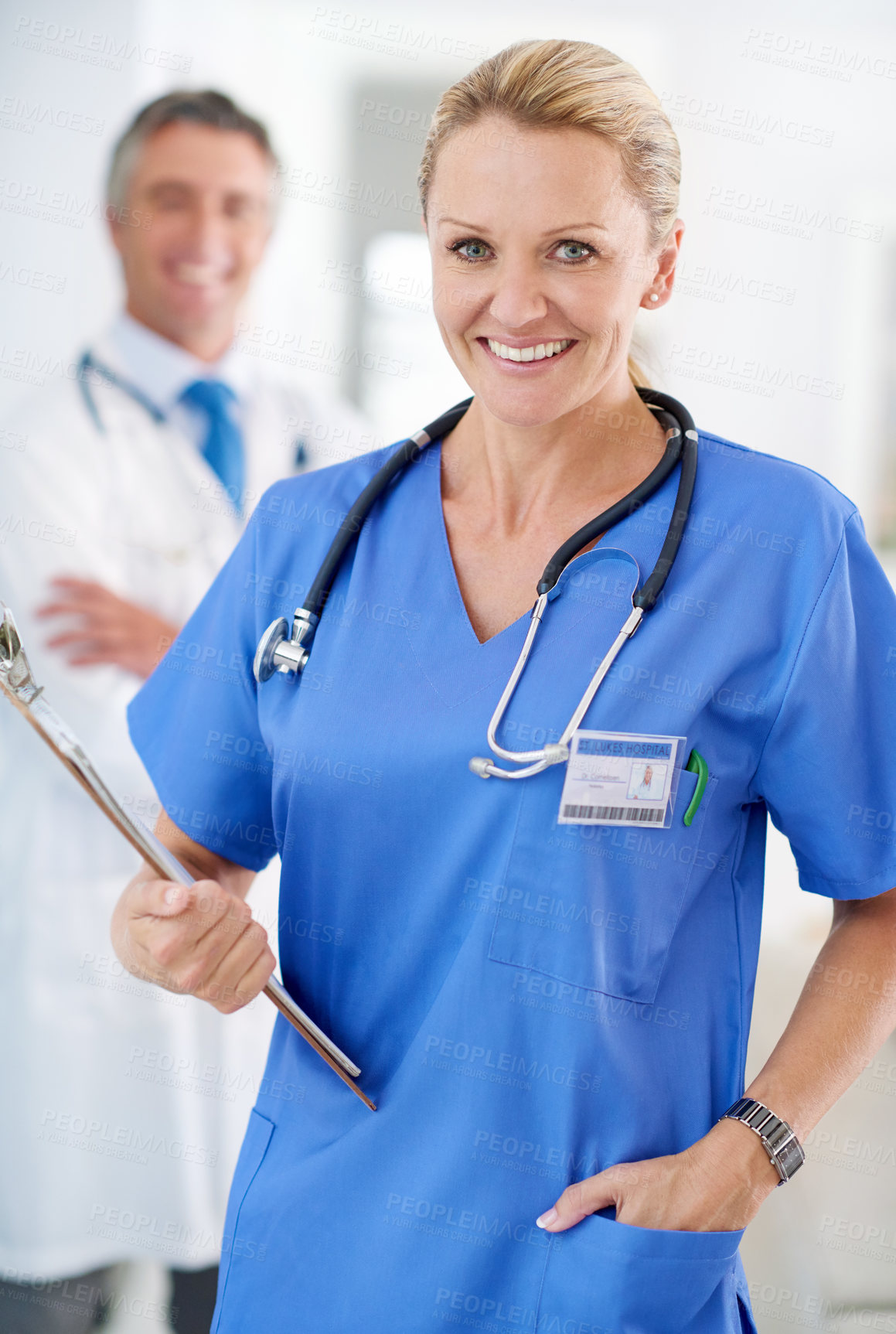 Buy stock photo Portrait of a female doctor in scrubs with a colleague standing in a the background