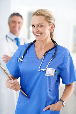 Buy stock photo Portrait of a female doctor in scrubs with a colleague standing in a the background