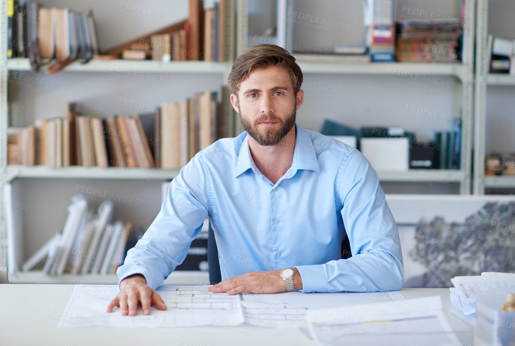 Buy stock photo Portrait of a handsome young architect sitting at his desk with blueprints in front of him