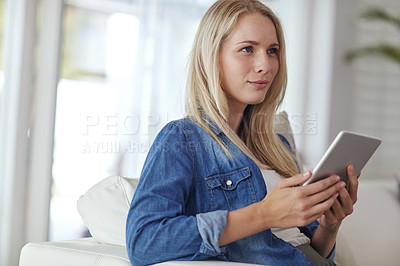 Buy stock photo Shot of a young woman using a digital tablet while sitting on her living room sofa