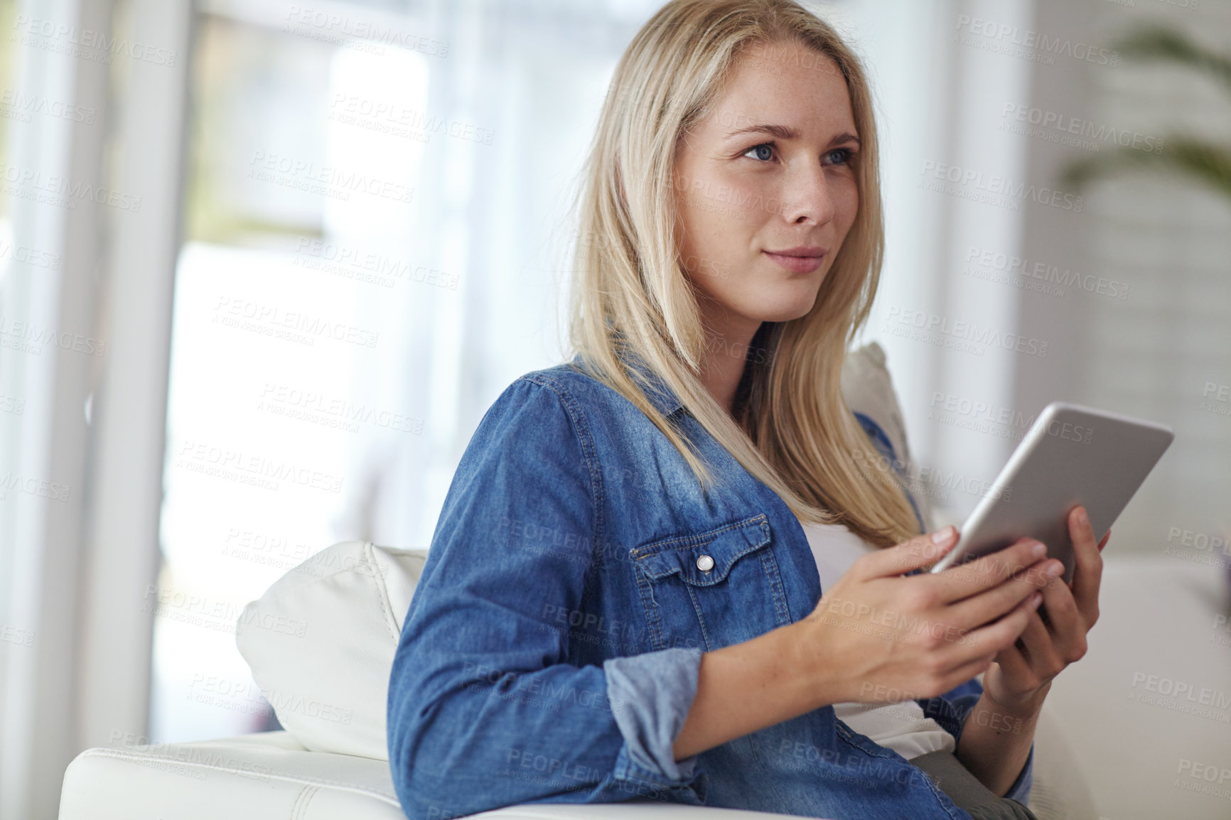 Buy stock photo Shot of a young woman using a digital tablet while sitting on her living room sofa