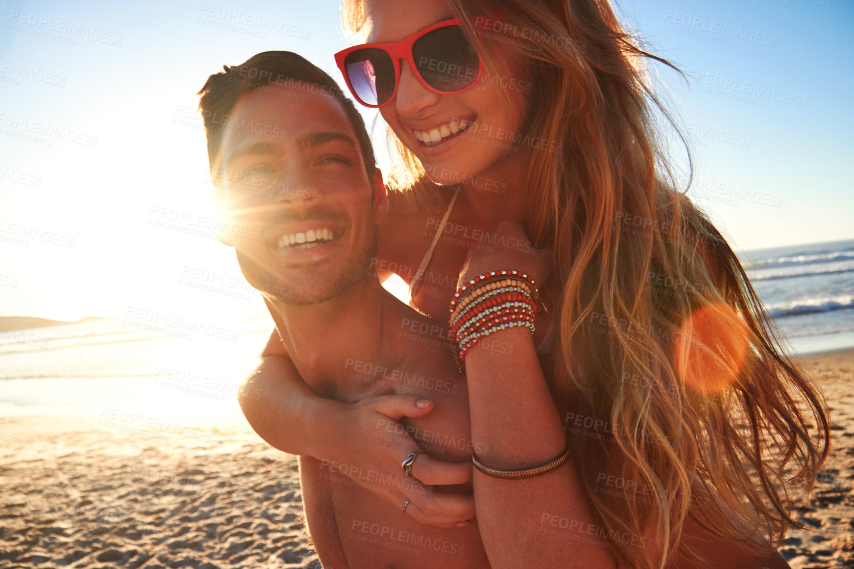 Buy stock photo Cropped shot of a young man piggybacking his girlfriend at the beach