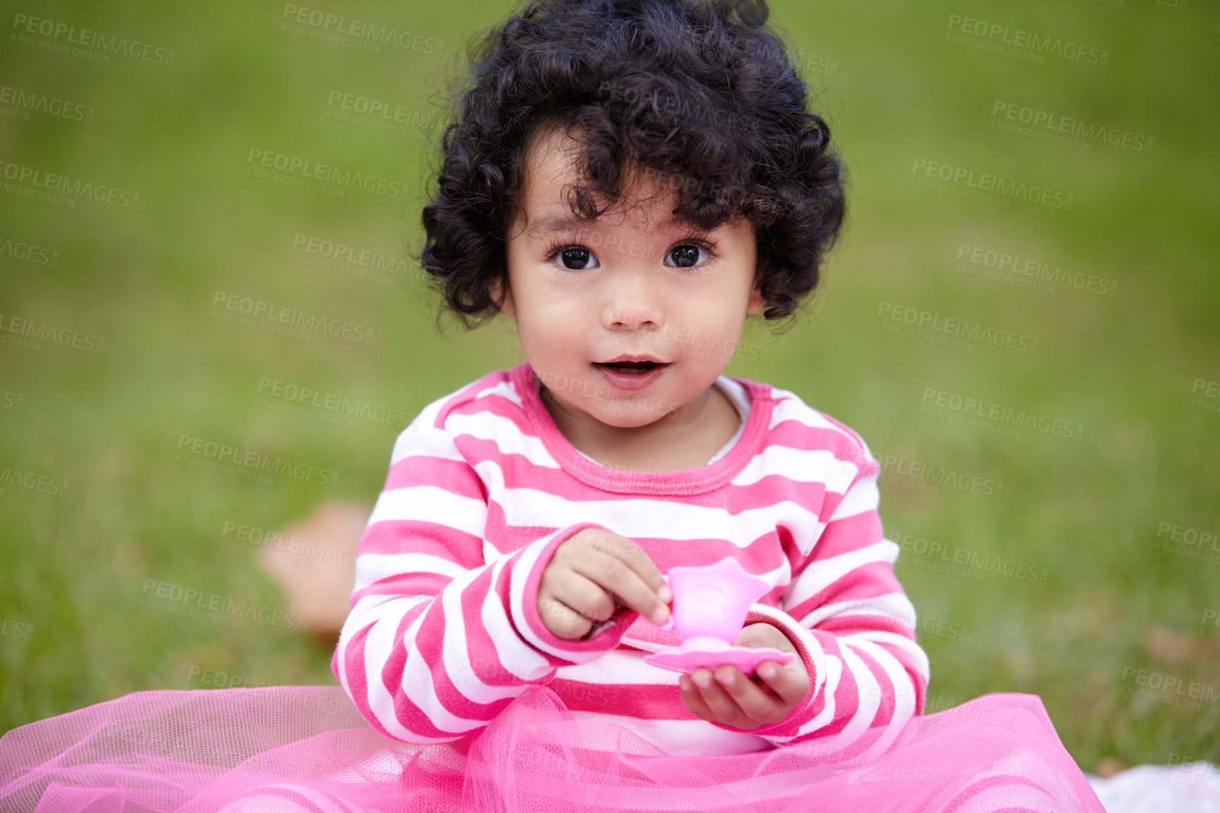 Buy stock photo Nature, portrait and girl kid in a garden play with toy on the grass on summer weekend. Adorable, playful and young child, baby or toddler with curly hair sitting on the lawn in outdoor field or park