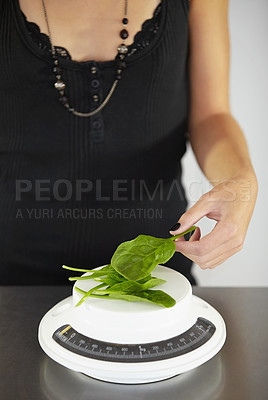 Buy stock photo Hand, scale and spinach in kitchen for diet, food or eating disorder with leaves for meal plan. Woman, mental health and vegetable leaf to lose weight with anorexia, bulimia or starving in home