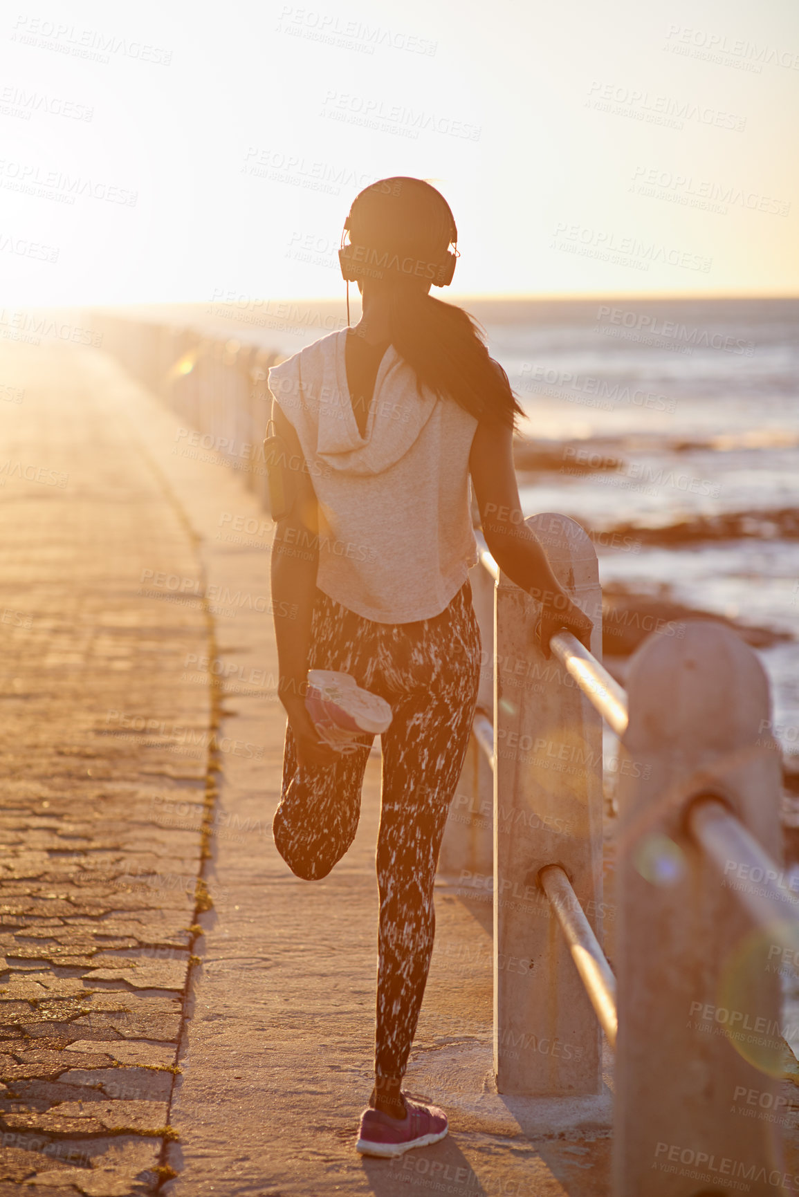 Buy stock photo Back, woman and stretching on beach outdoor for cardio performance, sports workout and fitness goal. Girl, runner and warm up with headphones, marathon training and listening to music for competition