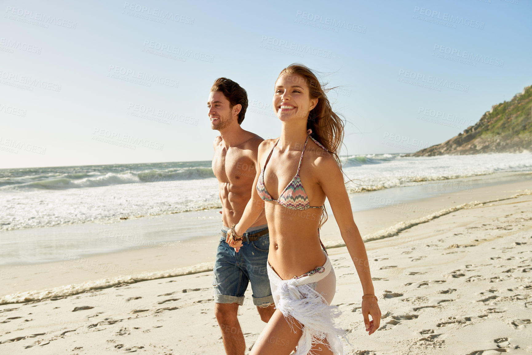 Buy stock photo Shot of a romantic young couple walking hand in hand on the beach