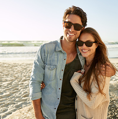 Buy stock photo Couple, beach and sunglasses with hug, happy or care with fashion, eye protection or vacation in summer. Man, woman and embrace with glasses for sun, trendy style or love by waves on tropical holiday