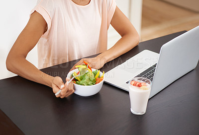 Buy stock photo Cropped shot of a young woman enjoying a salad and working on a laptop at home