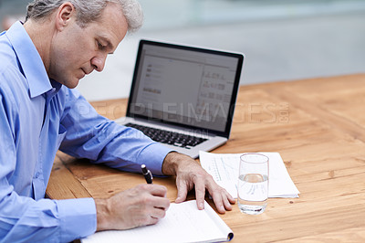 Buy stock photo Shot of a mature businessman writing notes at his desk in the office