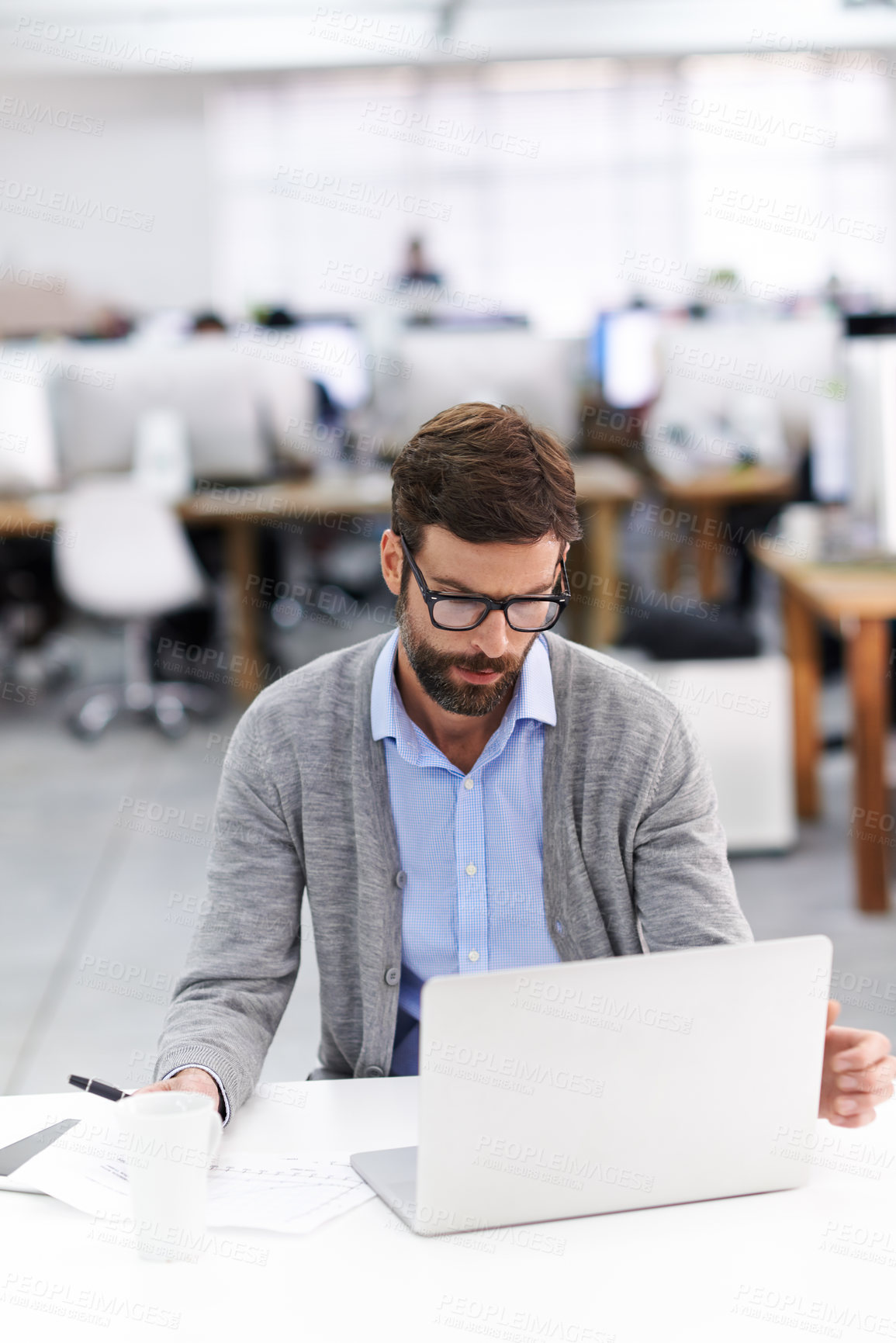 Buy stock photo Shot of a handsome young businessman using a laptop in a casual working environment