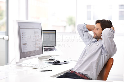 Buy stock photo Shot of a handsome young businessman reclining in his chair while using a computer in an office