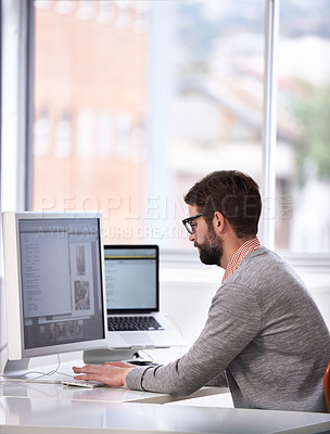 Buy stock photo Shot of a handsome young man working on a computer in a casual working environment