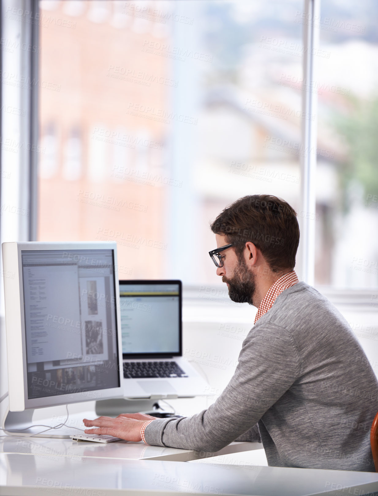 Buy stock photo Shot of a handsome young man working on a computer in a casual working environment