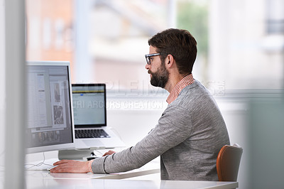 Buy stock photo Shot of a handsome young man working on a computer in a casual working environment