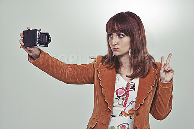 Buy stock photo Cropped studio shot of a young woman in a vintage outfit taking a selfie with an old-fashioned camera