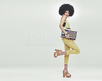 Buy stock photo A young woman wearing a 70s retro jumpsuit holding a cassette player and striking a disco pose