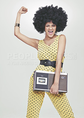 Buy stock photo A young woman wearing a 70s retro jumpsuit holding a cassette player and striking a disco pose