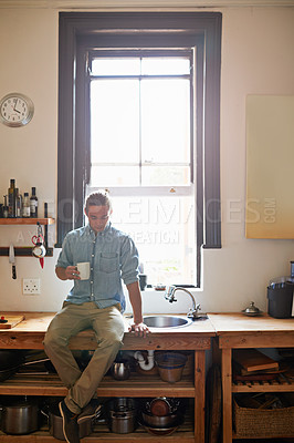 Buy stock photo Shot of a young man sitting on his kitchen sink counter