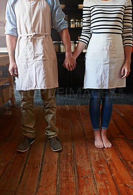 Buy stock photo Home, couple and holding hands with apron in kitchen for cooking support, love and bonding with baking. People, feet and culinary relationship in house for commitment, loyalty and trust with floor