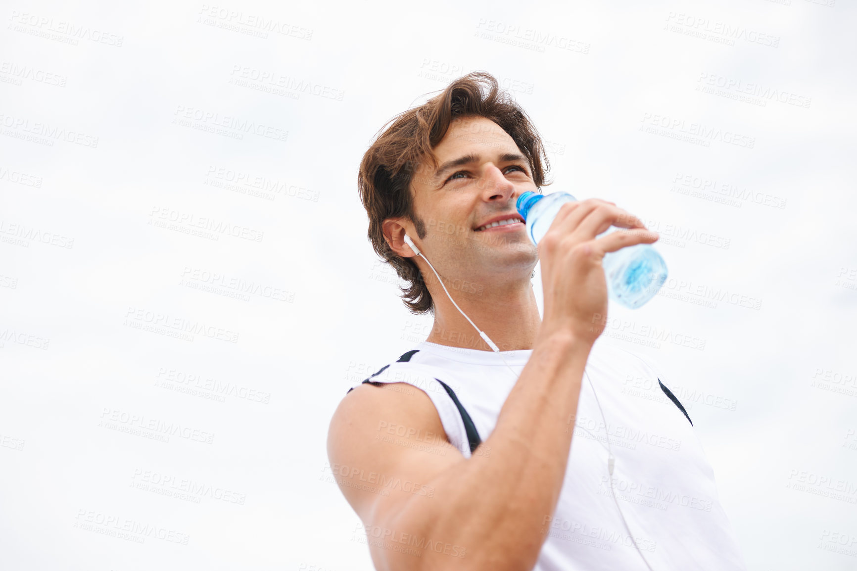 Buy stock photo Man, smile and drinking water on break from workout, earphones and hearing music, podcast or song on run. Male athlete, thirsty and hydrated for exercise, cardio and fitness outdoor with mockup
