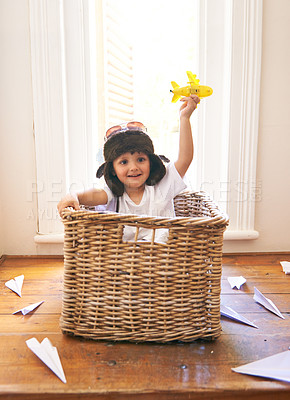 Buy stock photo Child, smile and airplane toy in home, playful and freedom of youth with paper for fun and games. Little kid, happiness and hand in air with body in basket with hat on head as helmet with imagination