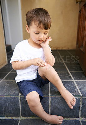Buy stock photo Small child, injured and bleed on knee from fall, scratch and youth in pain from bruise on leg. Young boy, sitting and stairs outdoor house, looking and wound on skin from accident, touch and hand