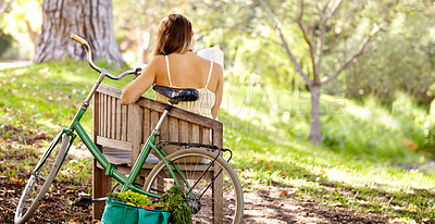Buy stock photo Rearview shot of a young woman sitting on a bench with her bicycle behind her