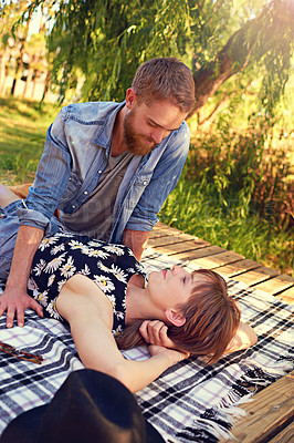 Buy stock photo Shot of an affectionate young couple lying on a blanket outdoors